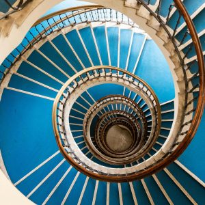 Lange Wendeltreppe, die nach unten geht mit blauem Teppich und weißem Geländer