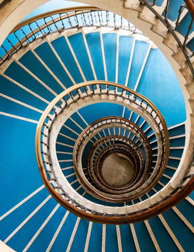 Lange Wendeltreppe, die nach unten geht mit blauem Teppich und weißem Geländer